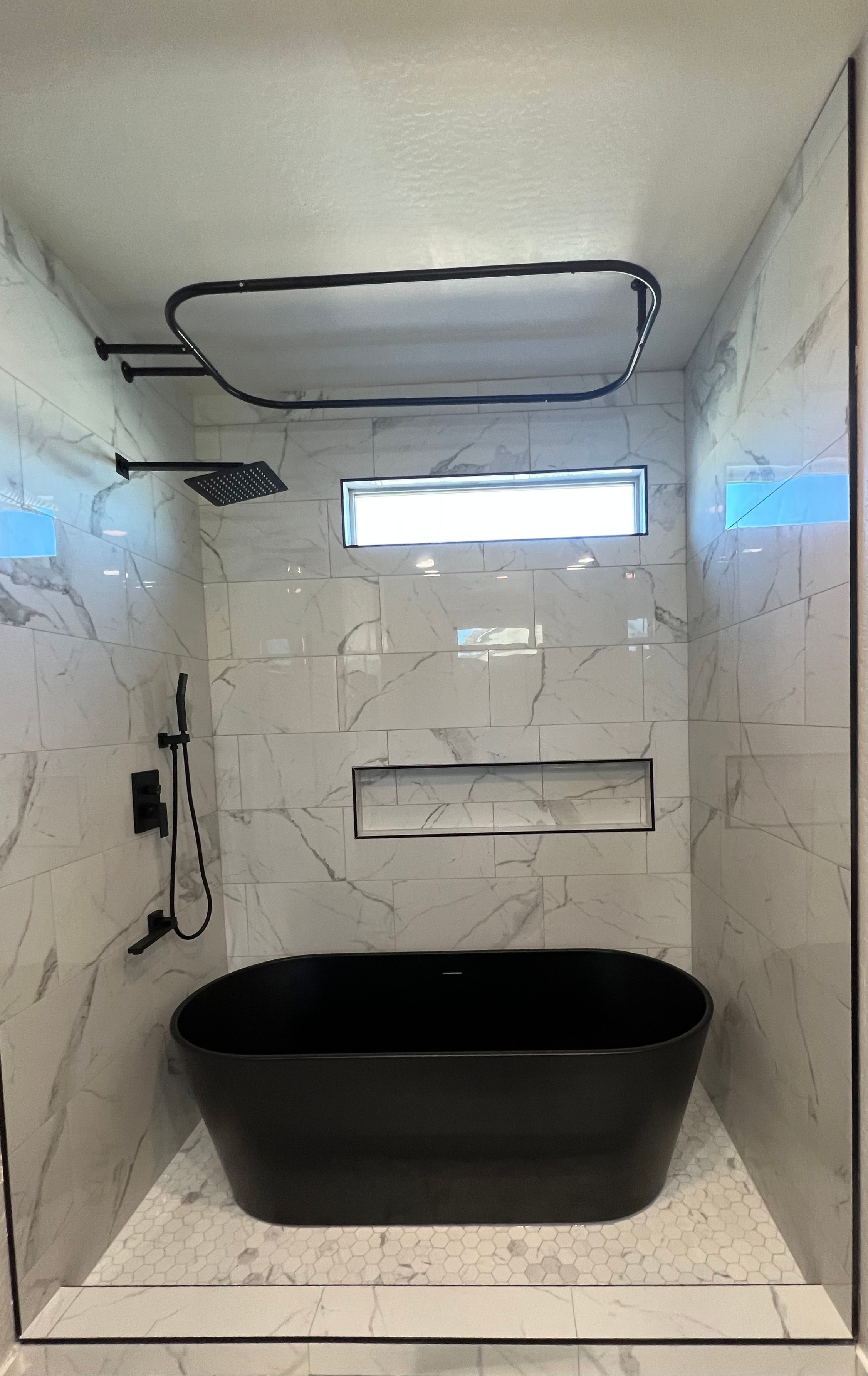 Luxury bathroom with black freestanding soaking tub, marble tile walls, and rain shower head