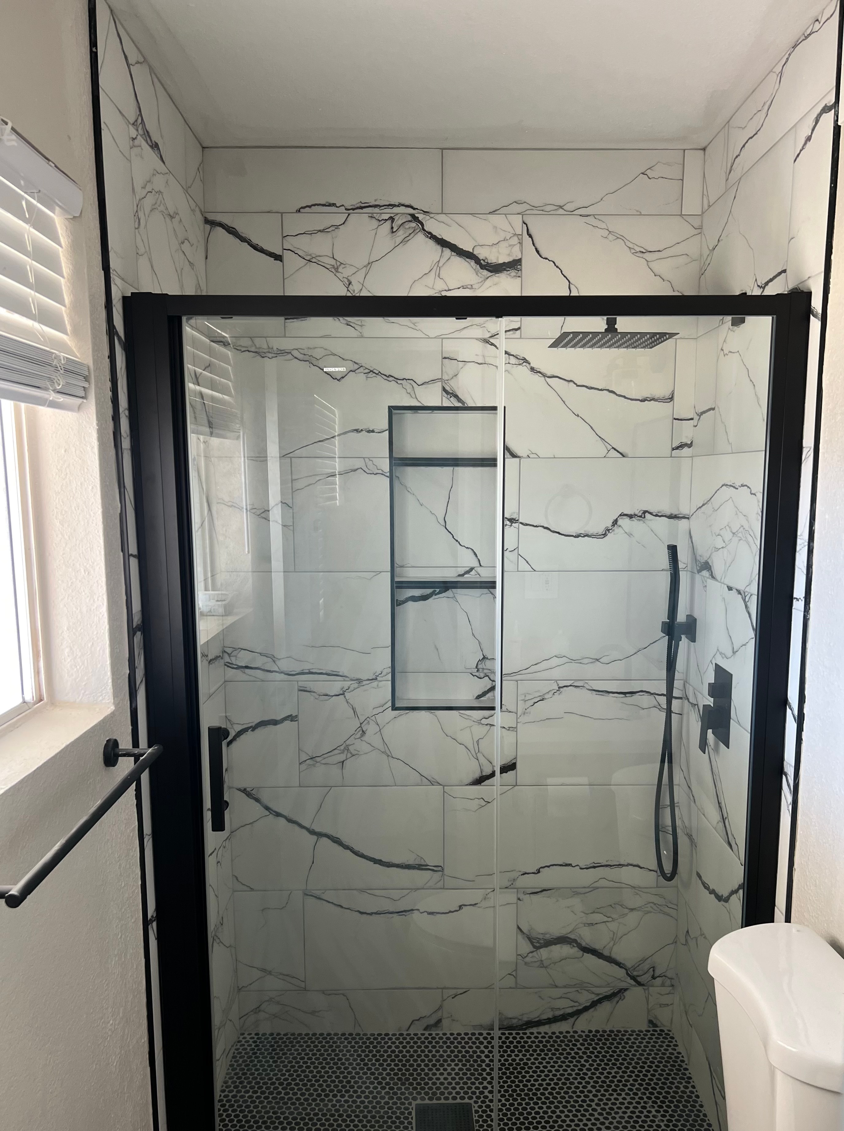 Bathroom shower remodel with white marble tile and black fixtures